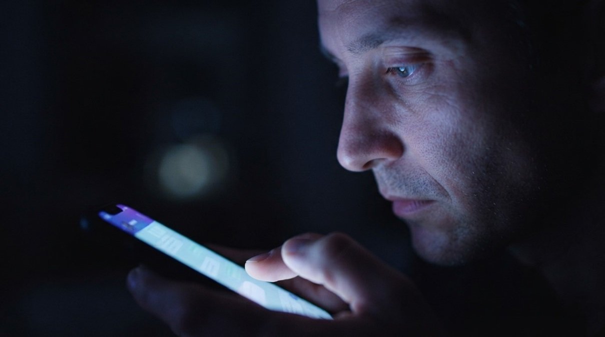 A close-up cinematic photograph of a smartphone screen reflecting light onto a user's face during AI interactions.